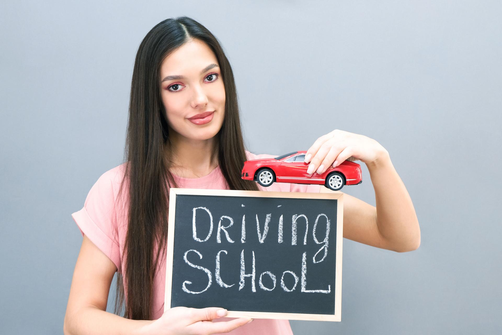 Driving school idea and concept, student driver passed the exam, drivers license, portrait of a beautiful happy young woman, holding a car in her hand. on a gray isolated background.