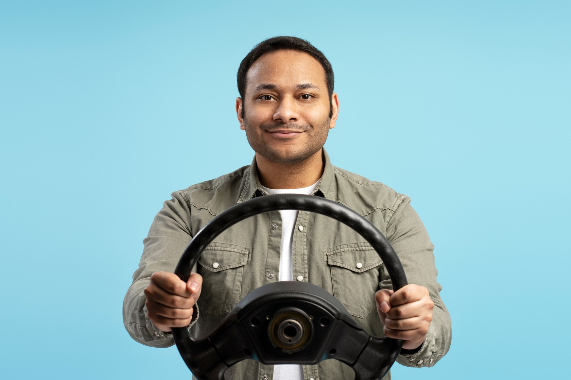 Smiling man holding steering wheel on blue background